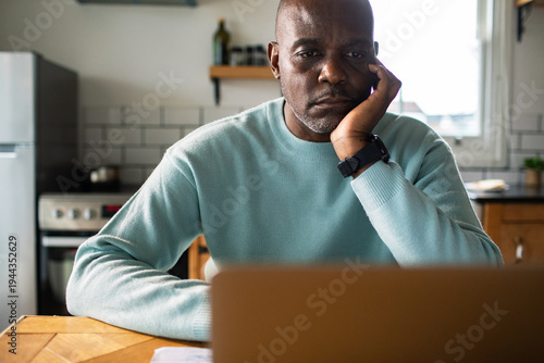 Concerned man working on laptop in home kitchen