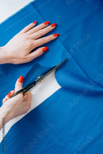 Fotografía Close-up of hands cutting blue fabric along pattern line with black scissors
