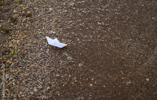Small paper boat resting on wet sand at the beach, childhood nostalgia, minimal seaside background, travel and freedom concept, calm mood.