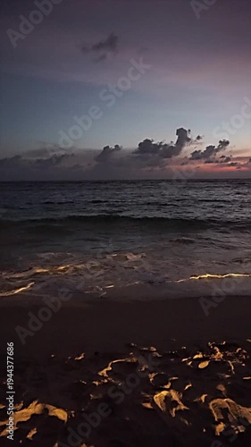 Ocean waves reaching the sandy beach during a calm sunset with clouds on the horizon.