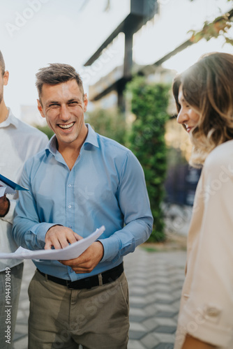 Business professionals smile while reviewing papers outdoors. People stand outside discussing documents on a bright spring day.
