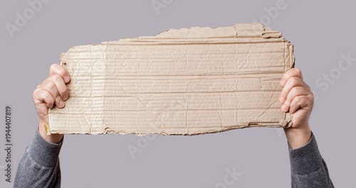 Close up hand holding an empty cardboard sign. Hand raised up, holding a blank piece of cardboard for writing against. Protest or warning. The blank space, can be used to add text or a symbol, carton