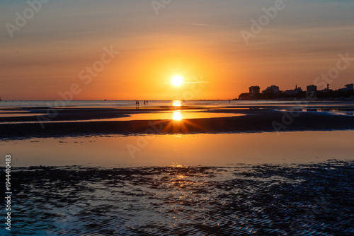 Sunset at sea with lonely walkers. Minimalist coastal landscape with calm sea and setting sun in the background.