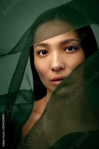Canvastavla Beauty portrait of Asian woman looking through translucent green silk fabric expressing curiosity, individuality and modern fashion aesthetics for cosmetics advertising and editorial design