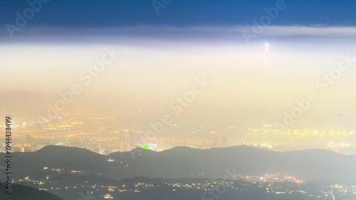 A stunning night view of Taipei city from Datun Mountain, featuring city lights glowing through thick fog and clouds.