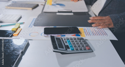 business documents on office table with tablet, smart phone and laptop and two colleagues discussing data