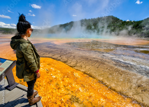 Tableau sur toile A woman stands on a bridge looking at a yellow and green lake
