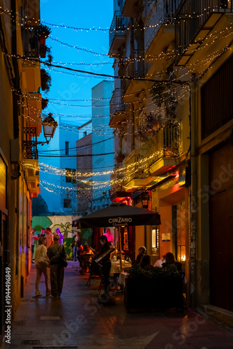 Cozy European street scene at dusk with string lights, people dining outdoors, and vibrant ambiance. Perfect for travel, nightlife, and urban lifestyle inspiration.