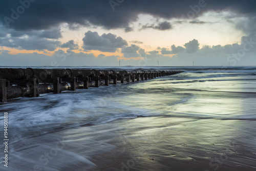Dawn, sunrise. Cambois Beach, Northumberland, England, UK. On a winter morning with heavy clouds in the sky and catching colour from the rising sun.