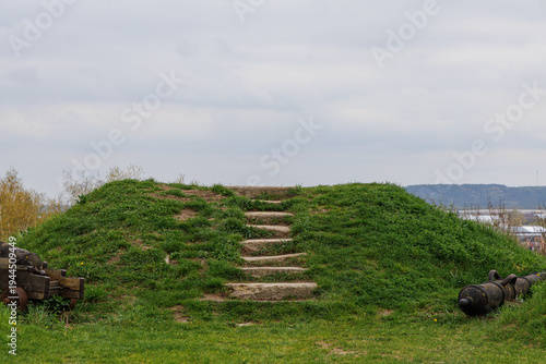 Historic fortress earthwork with cannons and stairs on grassy hill