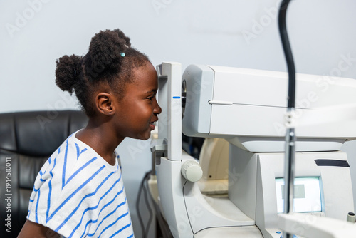 Fotografie Young African girl child receiving an ocular examination using autorefractor mac