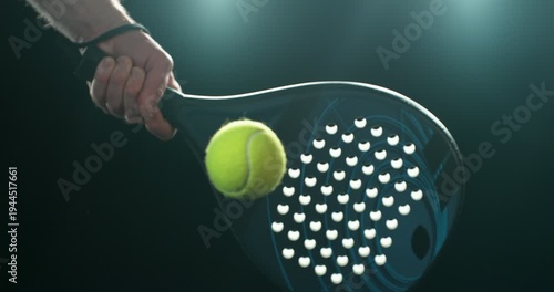 Super slow motion close-up of a hand holding a padel racket as a yellow ball hits the surface, filmed at 1000 fps. Dramatic studio lighting highlights the impact, motion of the racket and ball.