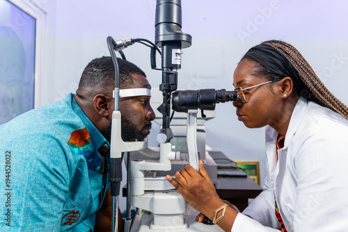 Bild auf Leinwand African female optometrist examining a male patient's eyes with a slit lamp mach