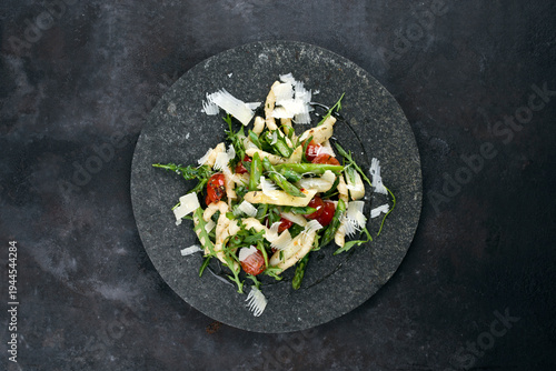 Cold vegetarian pasta noodle salad with green and white Asparagus tips, arugula, fresh tomatos and parmesan served as top view on a black stone plate
