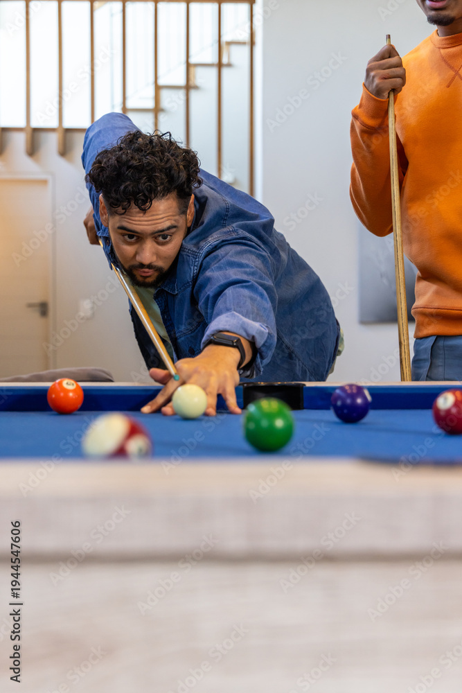 Fototapeta premium Diverse males lining up pool shot at blue felt table in home with cues, billiard balls