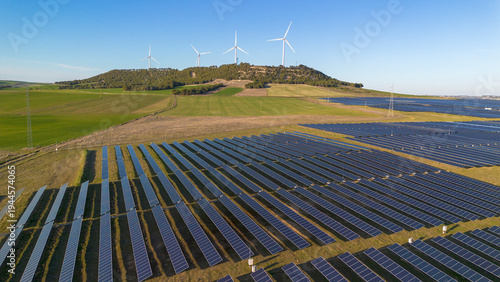 Aerial panorama of solar farm with wind turbines producing renewable energy