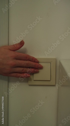 Close-up of hand turning wall light switch on and off in modern residential interior, controlling lighting for energy-efficient home comfort.