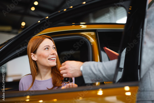 Obraz na płótnie Woman receiving car key from salesman while sitting in vehicle at dealership