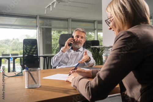 Female client signing agreement with lawyer as man makes business call