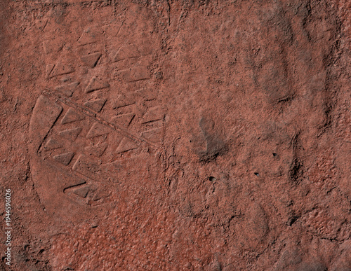 Shoe boot sole imprint on red grunge cement walkway becomes a rough texture rust orange background for adventures outside.