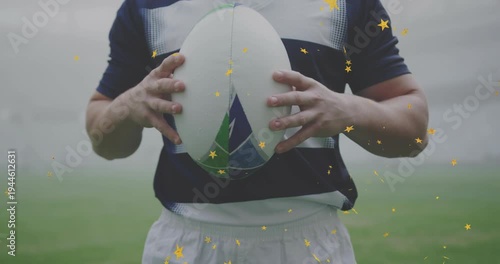 Rugby player adjusting grip, lifting ball to chest on misty sports pitch, golden stars showing pass