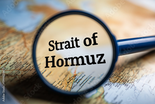 Magnifying glass focusing on Strait of Hormuz on world map for geopolitics and global trade concept