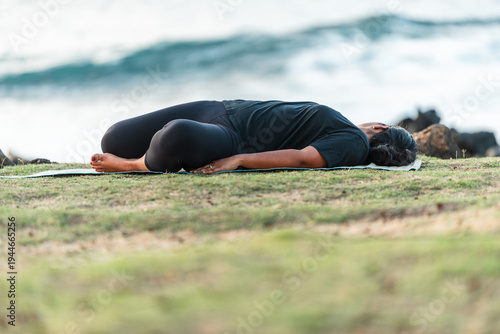 Bild auf Leinwand Woman practicing a reclining supine twist yoga pose on a mat by the ocean