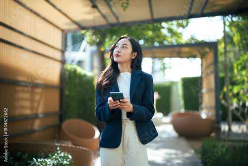 Young Asian businesswoman holding smartphone looking up outdoors