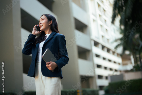 Young Asian businesswoman talking on smartphone holding tablet