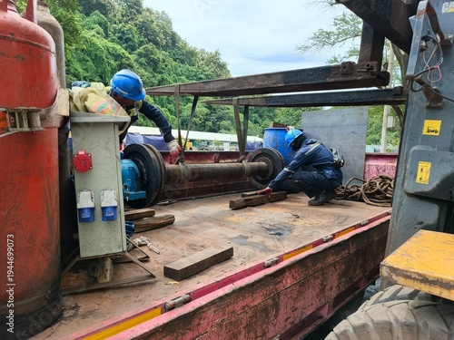 Industrial workers using a forklift and webbing slings to carefully lift a tripper conveyor axle for maintenance. 