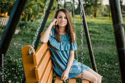 Tableau sur toile Young woman relaxing on wooden swing in summer park