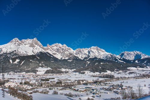 Snow covered Steinernes Meer mountain range rising above the winter valley of Saalfelden in Austria under a clear blue sky