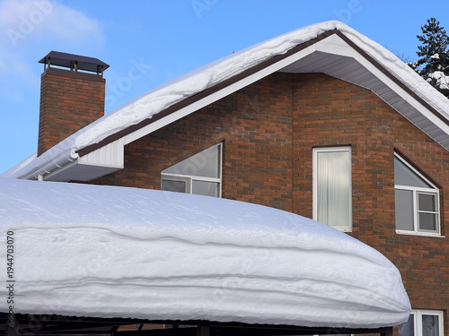 Residential brick house exterior in winter, covered with thick snow on the roof and carport, showing cold weather conditions