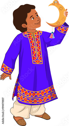 A young boy holds a crescent moon decoration while wearing traditional clothing indoors.