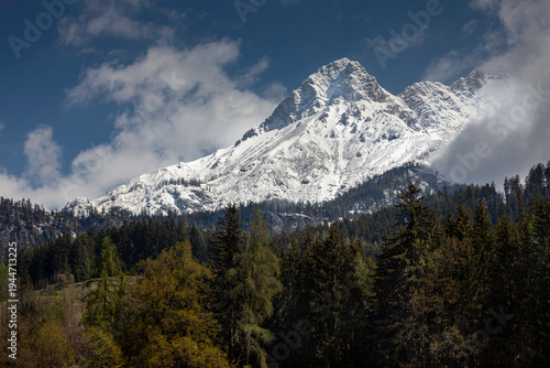 Snow-covered mountain peak of the steinernes meer range in the northern limestone alps during spring with a green pine forest foreground and dramatic clouds