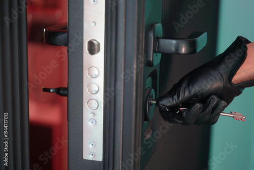 Person in black leather glove unlocking residential door with keys. Concept of theft, break‑in, hidden identity, illegal access to property, squatter intrusion and tense unknown entry. Photo