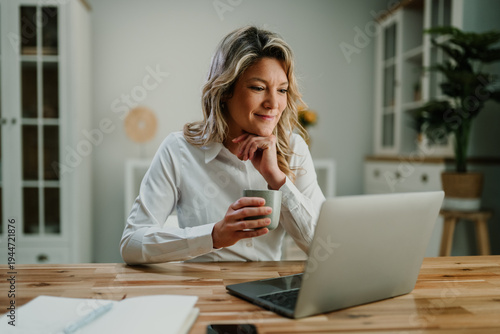 Foto Woman working remotely on laptop at home office, enjoying coffee while telecommu