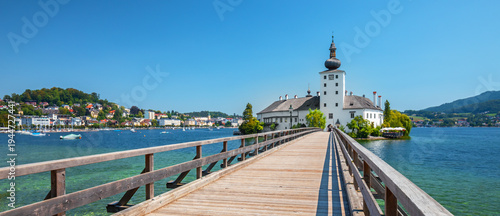 Scenic view of Ort Castle on Lake Traunsee in Gmunden, Upper Austria. Historic lakeside castle connected by a wooden bridge, surrounded by alpine landscape and calm water, a popular travel destination