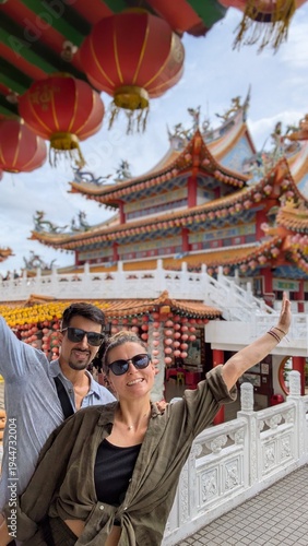 Caucasian couple taking selfie together at colourful chinese temple terrace in Kuala Lumpur Malaysia, smiling two people visiting famous historical taoism attraction with dragon mythology and cultural