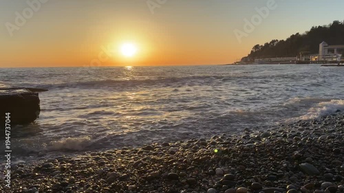 Sunset over Black Sea with waves rolling onto pebble beach and coastal hillside near Matsesta under warm evening light. Travel marketing, seaside tourism promotion, nature landscape storytelling