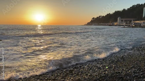 Sunset over Black Sea with waves rolling onto pebble beach and coastal hillside near Matsesta under warm evening light. Travel marketing, seaside tourism promotion, nature landscape storytelling