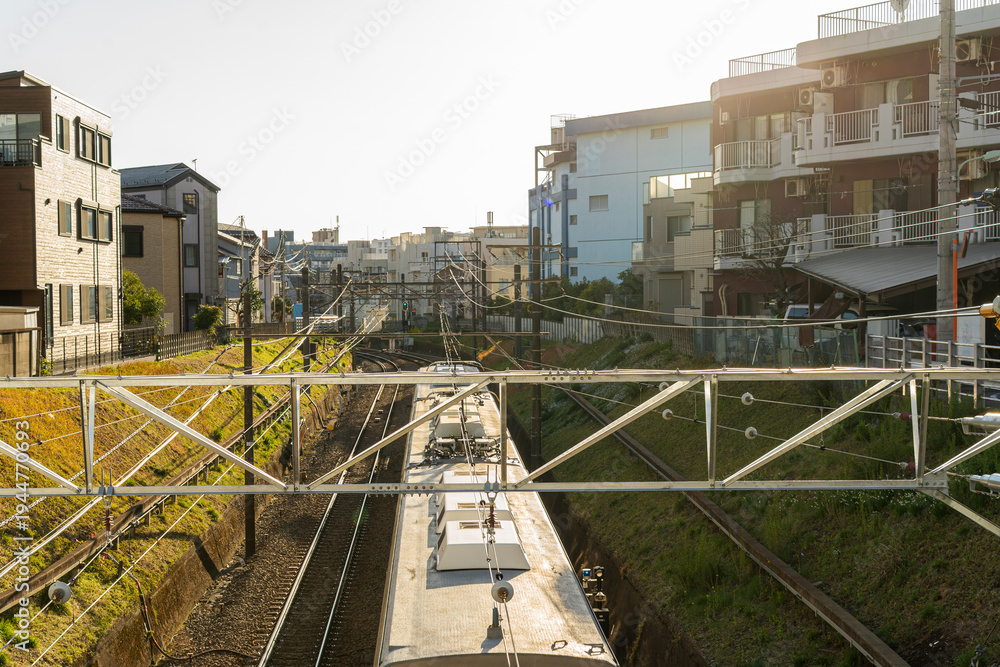 Fototapeta premium Commuter Train Passing Through Tokyo Residential Neighborhood Railway Tracks, Urban Public Transportation Infrastructure in Japan