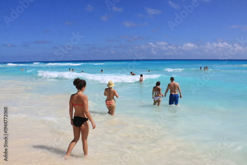 Group of beachgoers wading into turquoise ocean waves