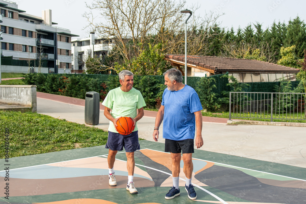 Obraz premium Two active senior men are enjoying a friendly game of basketball on an outdoor court, demonstrating healthy wellbeing and continuing sport life in their old age