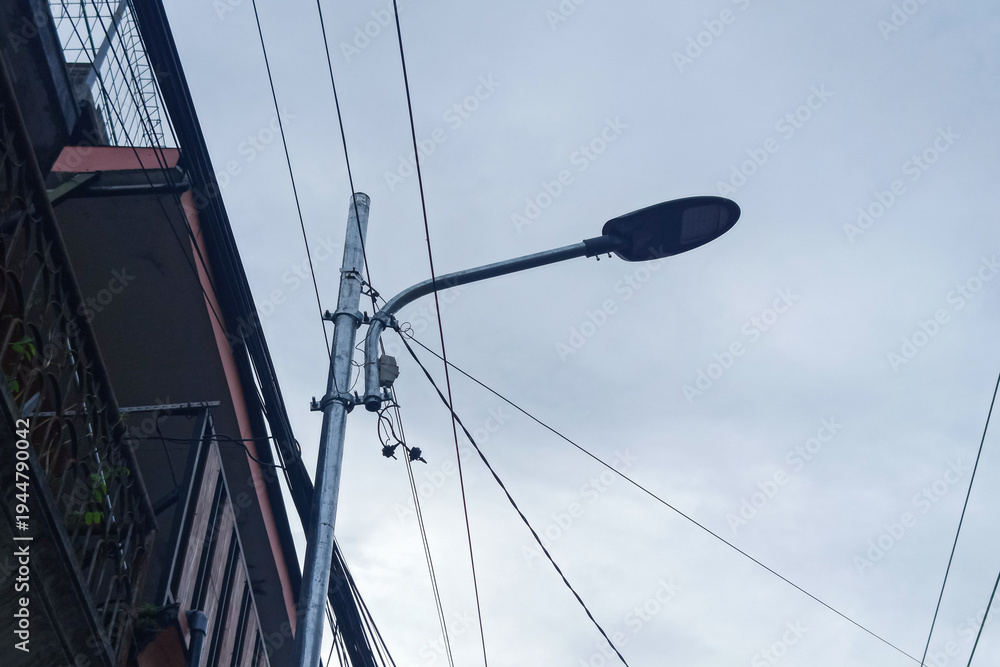 Fototapeta premium Streetlight pole with wires against a cloudy sky, urban scene