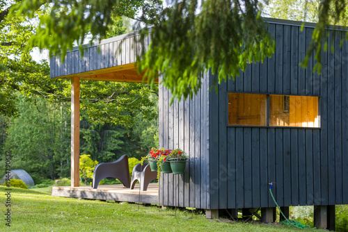 Modern wooden cabin with cozy porch and garden view in the countryside during sunny weather