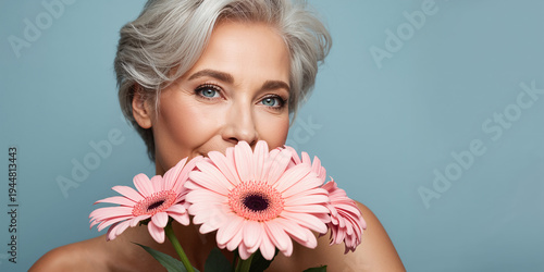 close-up of the face of a beautiful aging woman with gray hair and a gerbera flower
