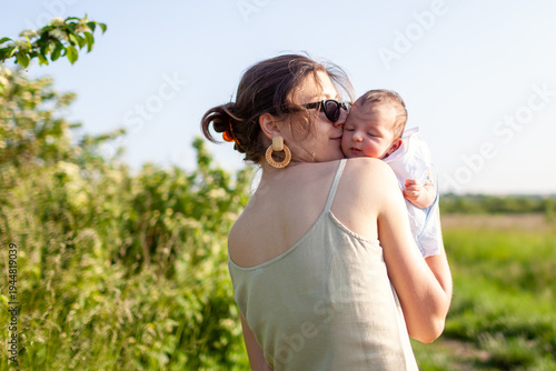 Mother's day. Young woman holding her newborn daughter walking outdoors. Little baby sleeping in mom's hands