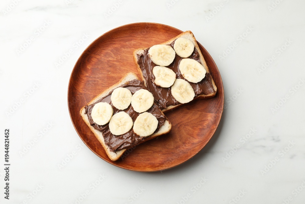 Fototapeta premium Toasts with chocolate paste and banana on white marble table, top view