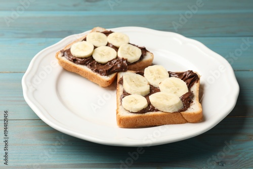 Toasts with chocolate paste and banana on light blue wooden table, closeup
